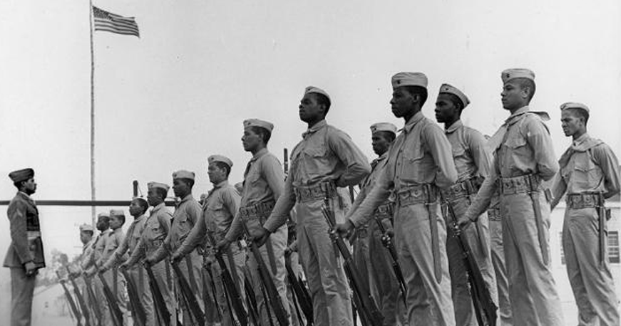 Montford Point Marines standing in formation beneath the American flag